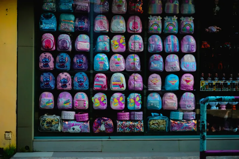 Row of colorful children's backpacks in pink, blue, yellow, and green hanging on display in a shop window