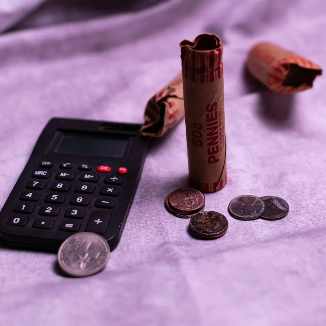 A penny roller and coins next to a small calculator.