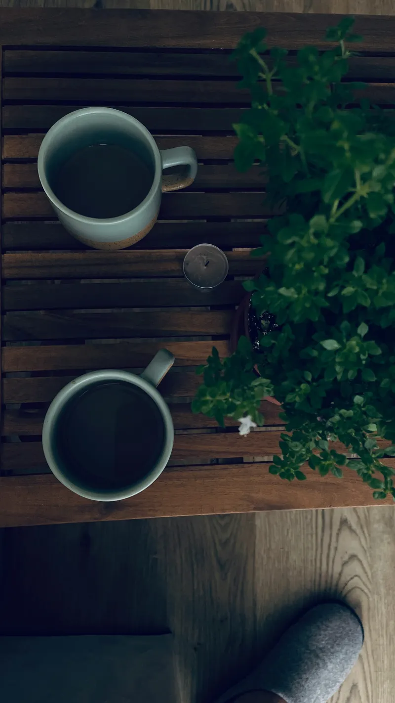 Two white ceramic coffee mugs side by side on a warm wooden table in soft morning light