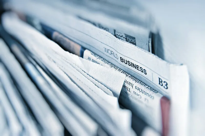 Close-up of a folded business newspaper page showing dense columns of printed financial data and small text in black ink on cream paper