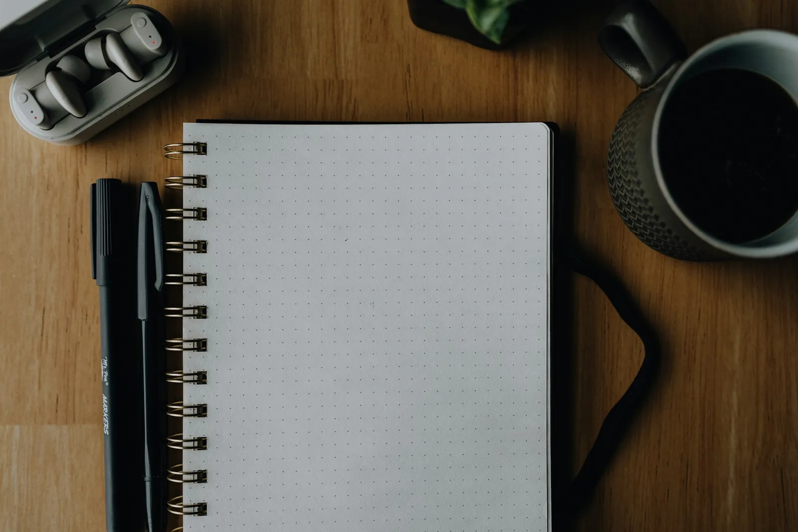 Flat-lay of an open notebook, ballpoint pen, headphones, and a cup of coffee arranged on a wooden desk