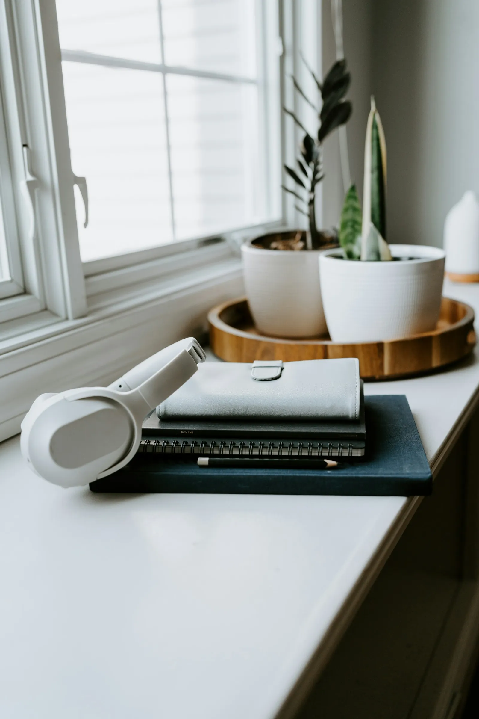 Open notebook on a wooden desk next to a small potted plant, a stack of books, headphones, and a pencil arranged on a clean workspace