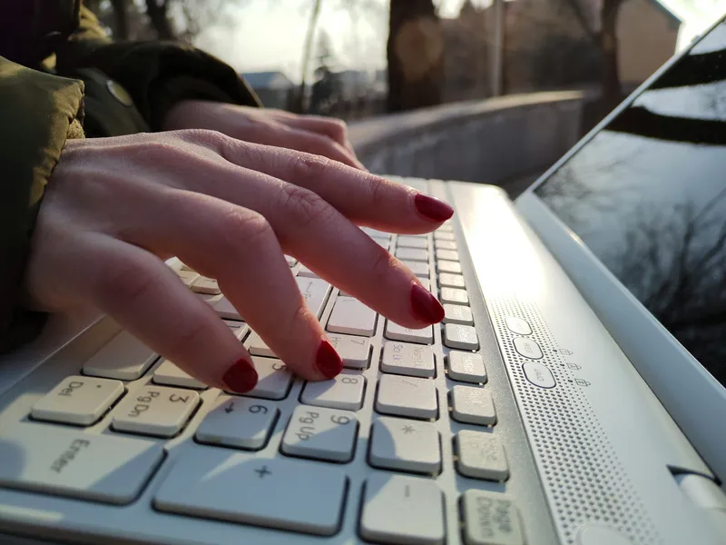 Close-up of a woman's hands typing on a laptop keyboard, with the laptop resting on her lap and the screen out of focus in the background