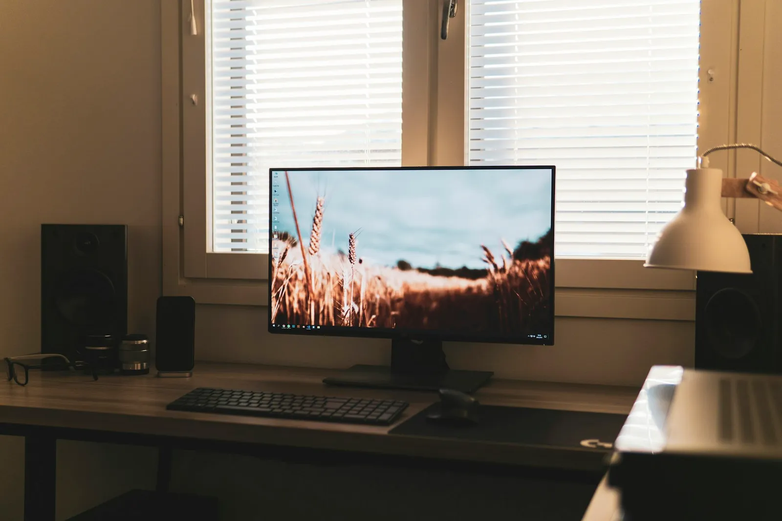 Computer monitor on a wooden home-office desk with a keyboard and warm natural light