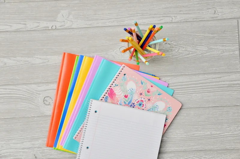 Pile of assorted-color notebooks stacked on a brown wooden table