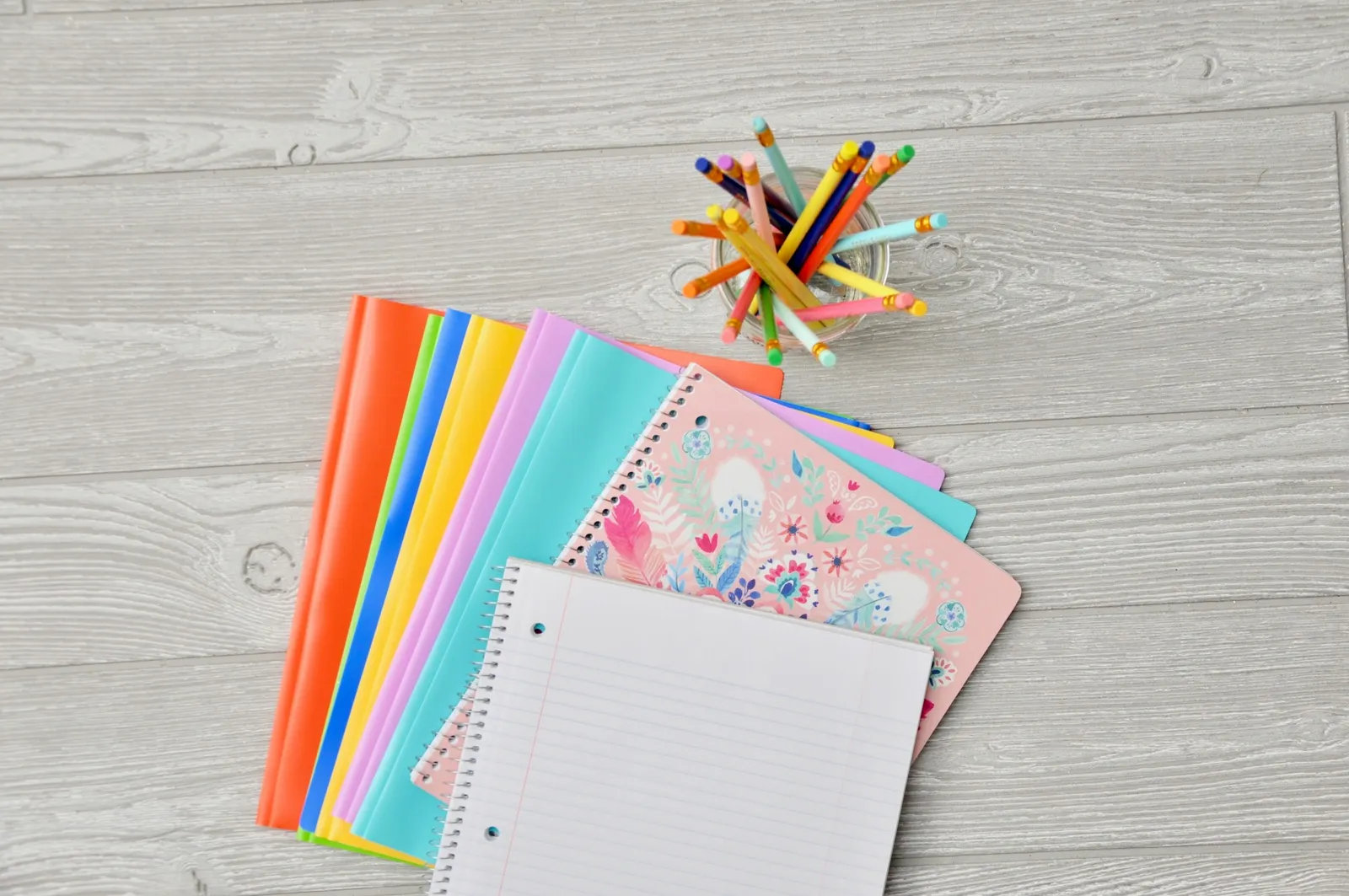 Pile of assorted-color notebooks stacked on a brown wooden table