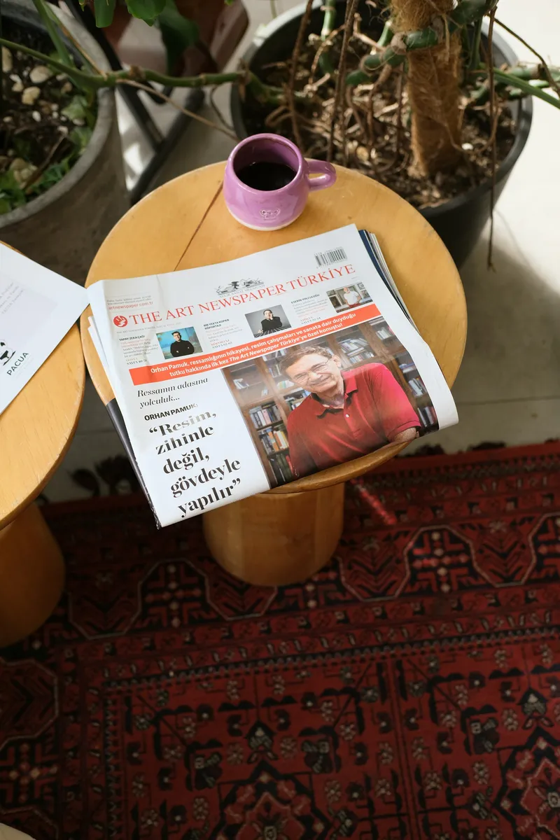 Folded newspaper resting on a wooden cafe table beside a white cup of coffee